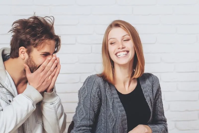 young handsome man laughing hard next to a woman near a white brick walls