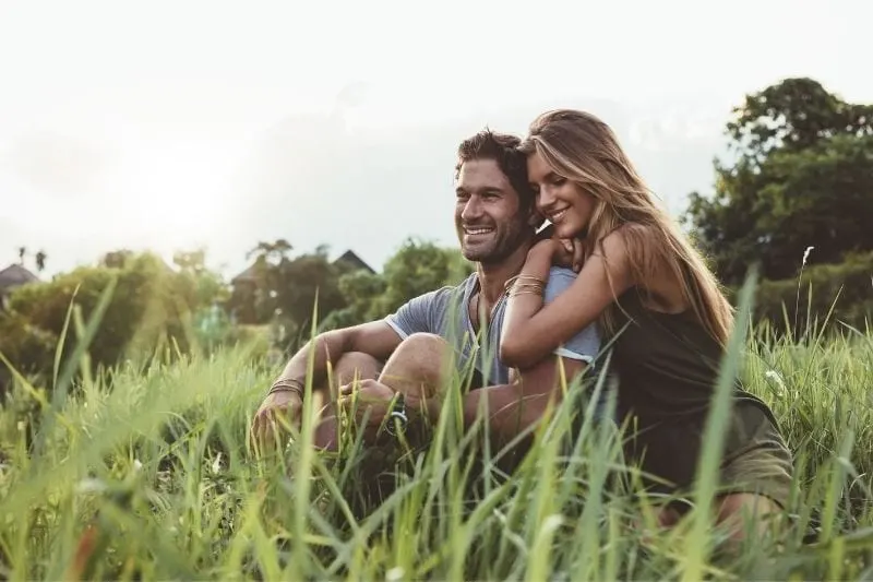 young happy lovers sitting in the meadows with the woman leaning on the man