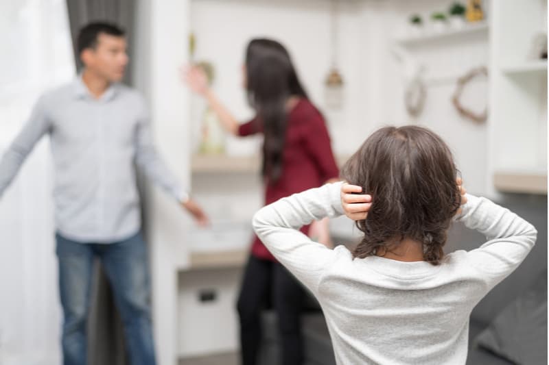 young kid covering ears looking at her parents fighting inside house