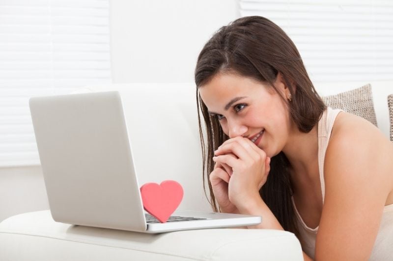 young woman giggling in front of the laptop with a heart on top of the keyboards