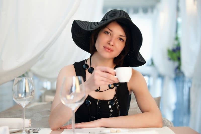 young woman in the restaurant sipping a cup of tea wearing black dress and hat