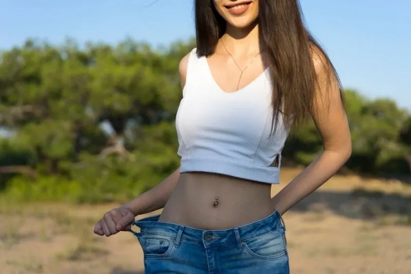 young woman losing weight showing old jeans loosely worn standing outdoors