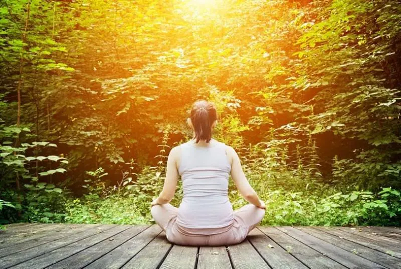 young woman meditates sitting on a wooden platform facing nature