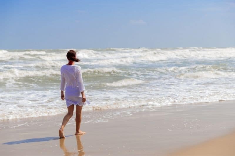giovane donna che cammina da sola sulla spiaggia con un vestito bianco