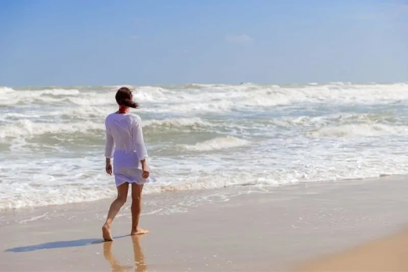 young woman walking alone by the beach wearing white dress