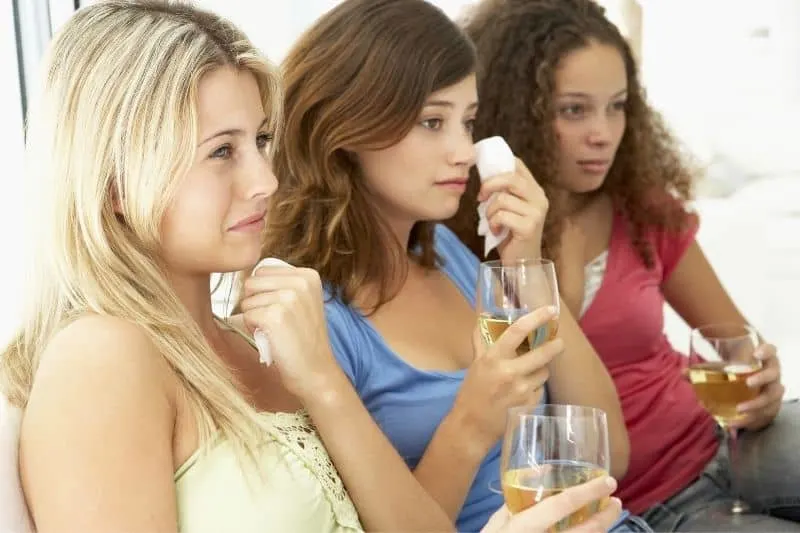 young women watching chick flick crying and holding wine glasses