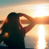 donna che guarda il nuovo giorno di fronte al sorgere del sole al mattino in piedi vicino a uno specchio d'acqua