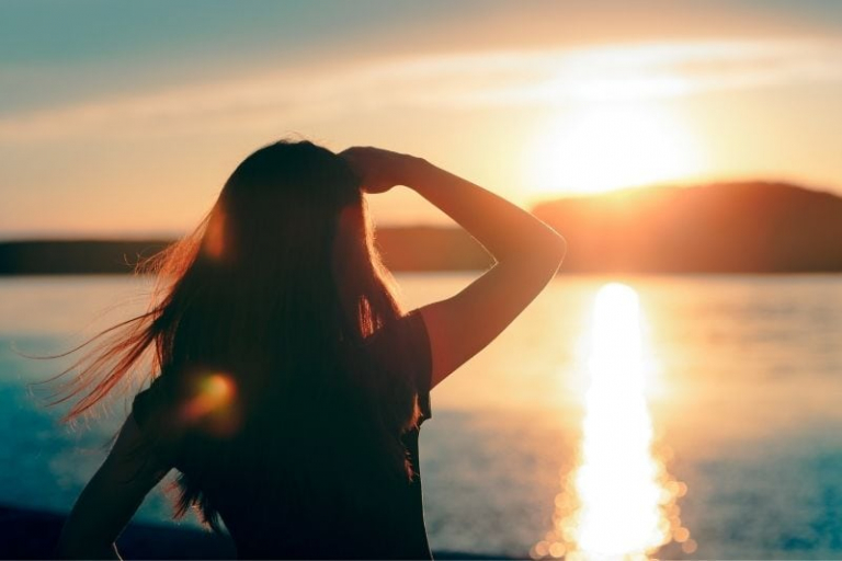 mujer mirando el nuevo día frente a la salida del sol en la mañana de pie cerca de un cuerpo de agua
