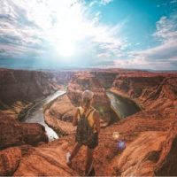 woman with backpack standing on top of canyon