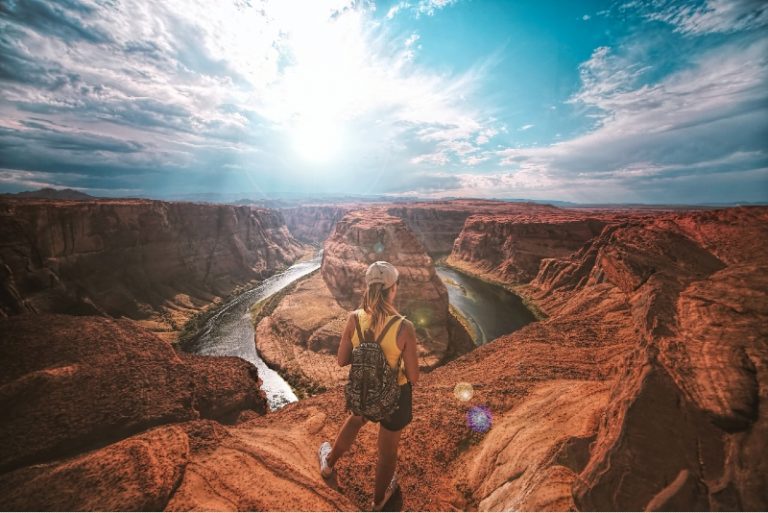 woman with backpack standing on top of canyon