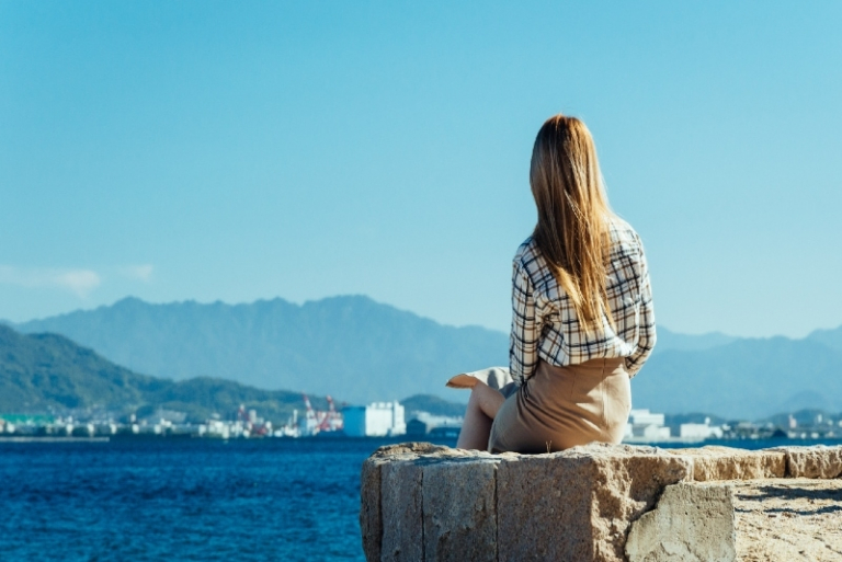 mujer sentada en muro de cemento mirando al mar