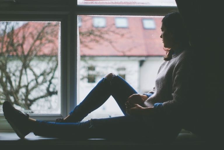 woman looking through window while sitting on window pane