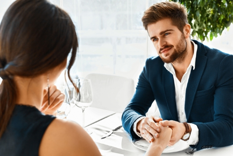 man holding woman's hand while sitting at table