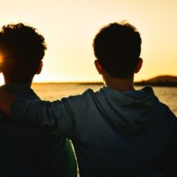 two men hugging while looking at sea