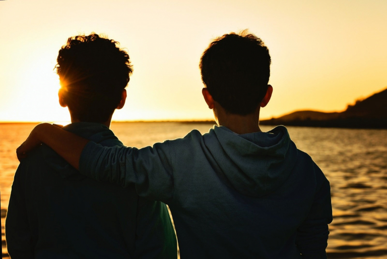 two men hugging while looking at sea