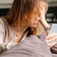 ragazza sconvolta sul letto che controlla il telefono