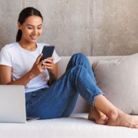 smiling woman sitting on couch and using her phone