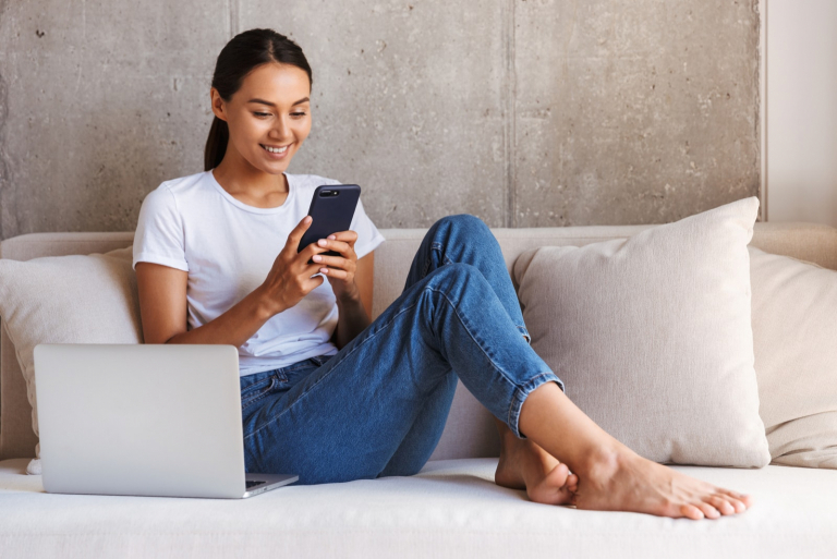 smiling woman sitting on couch and using her phone