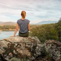 mujer con camiseta a rayas sentada en una roca mirando al lago