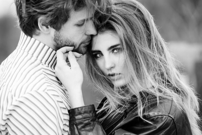 mujer con el pelo largo con estilo tocando la cara atractiva del hombre con barba en la fotografía en escala de grises