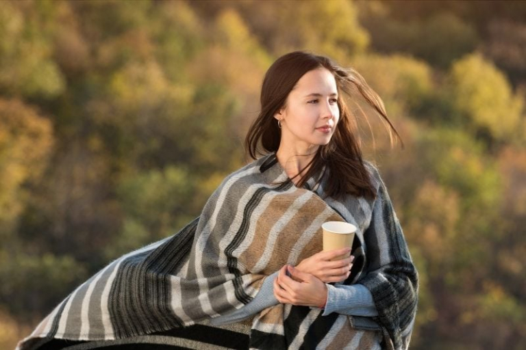 woman wrapped in blanket holding a cup of coffee walking outdoors