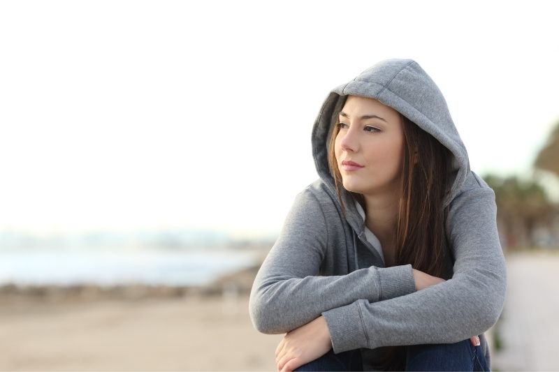 pensive woman sitting on the seashore wearing gray hoodies