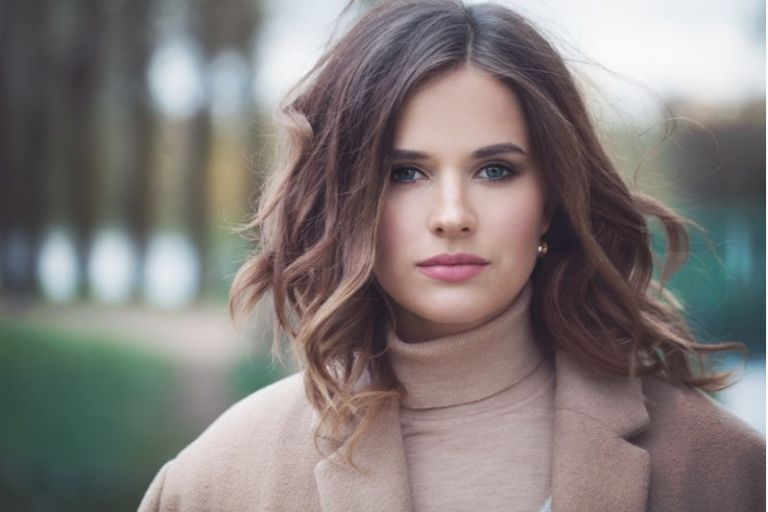 pretty woman wearing brown trench coat and standing outdoors staring at the camera