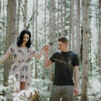 man holding woman's hand while standing in forest