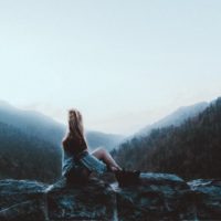 mulher sentada numa rocha a olhar para a montanha