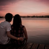 uomo e donna seduti su un molo durante il tramonto