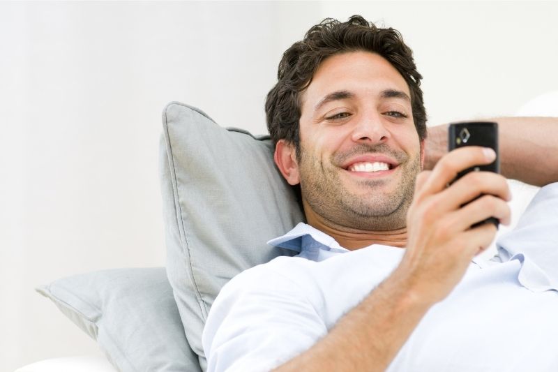handsome man lying down while texting on his smartphone