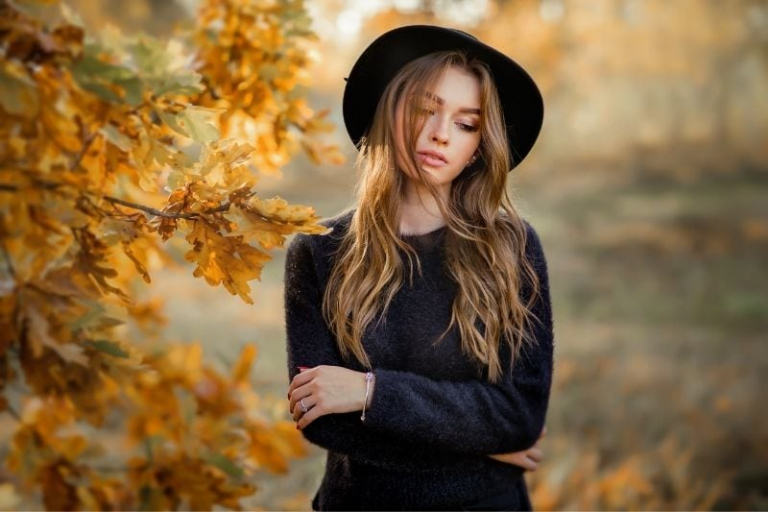 retrato de cerca de una mujer con un vestido oscuro cerca de las hojas de otoño
