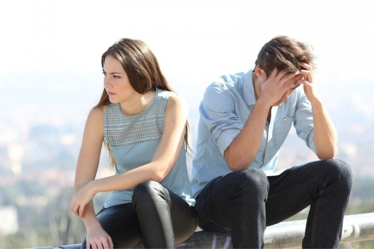 hombre y mujer disgustados sentados al aire libre con top azul y vaqueros negros