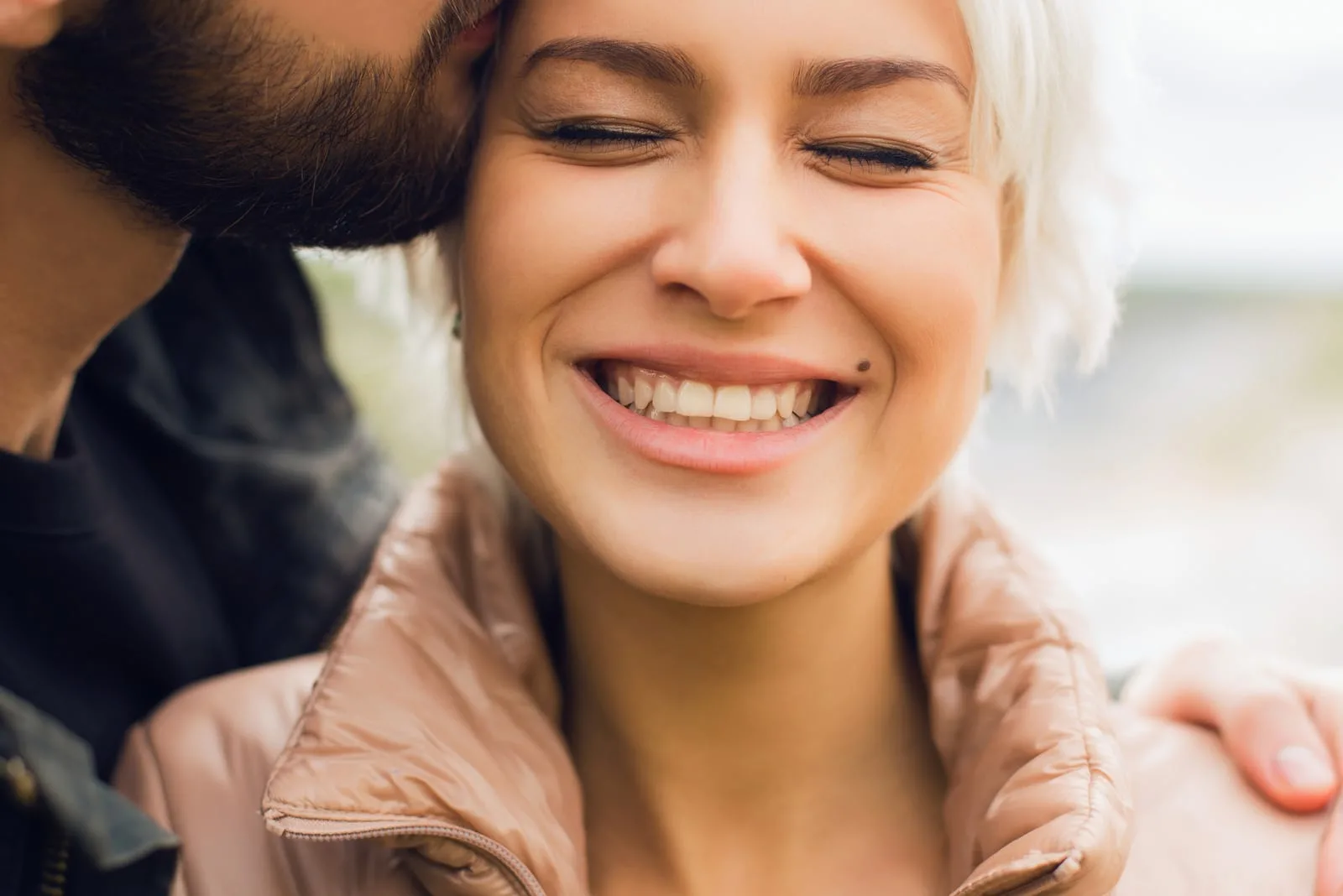 a bearded man kisses a smiling woman on the cheek