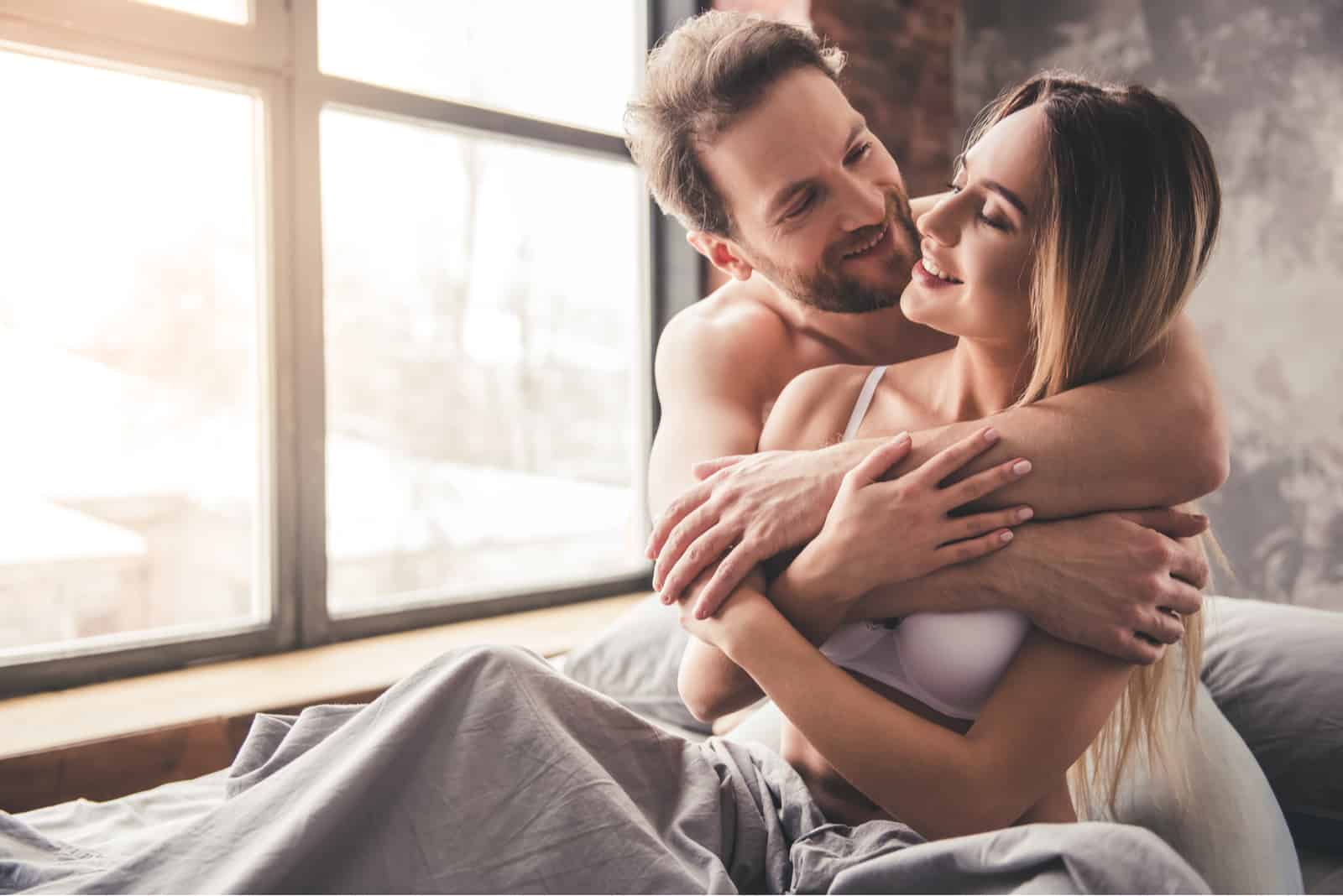 a smiling man and woman hugging in bed