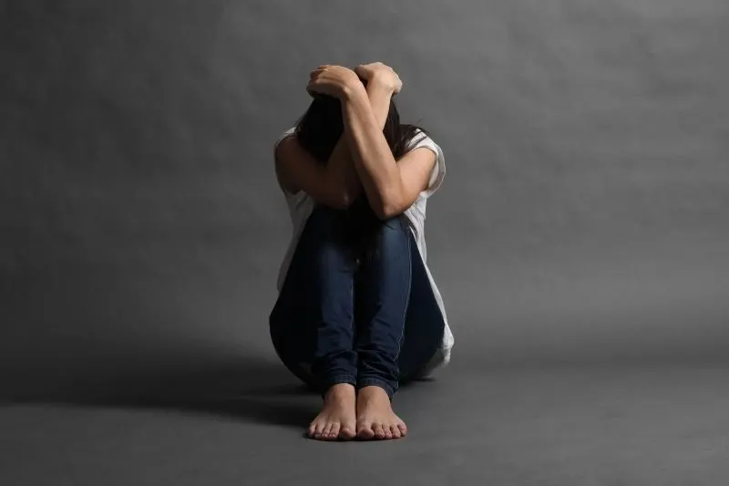 afraid depressed woman sitting on the floor tucked in with hands on head and head down