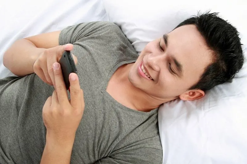 asian man reading message from his cellphone while laying down