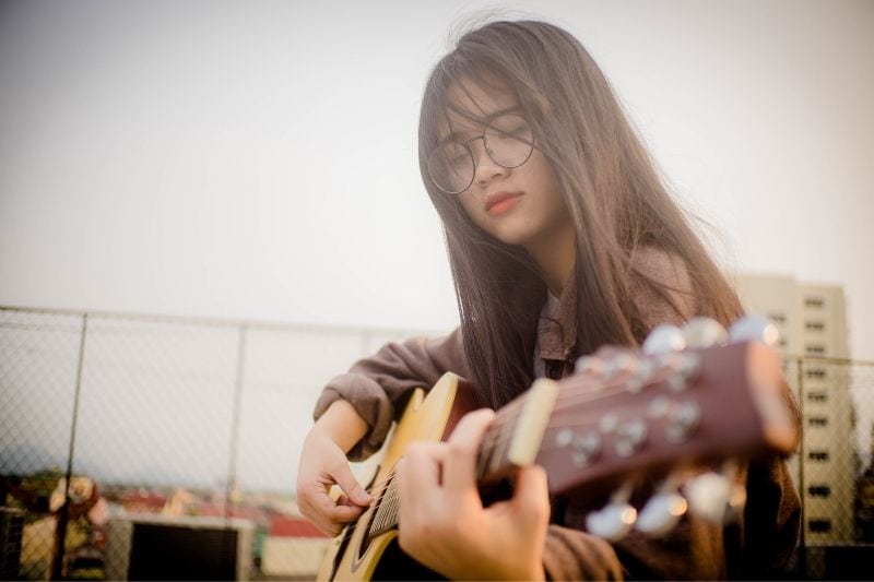 donna asiatica che suona la chitarra all'aperto con gli occhiali da vista