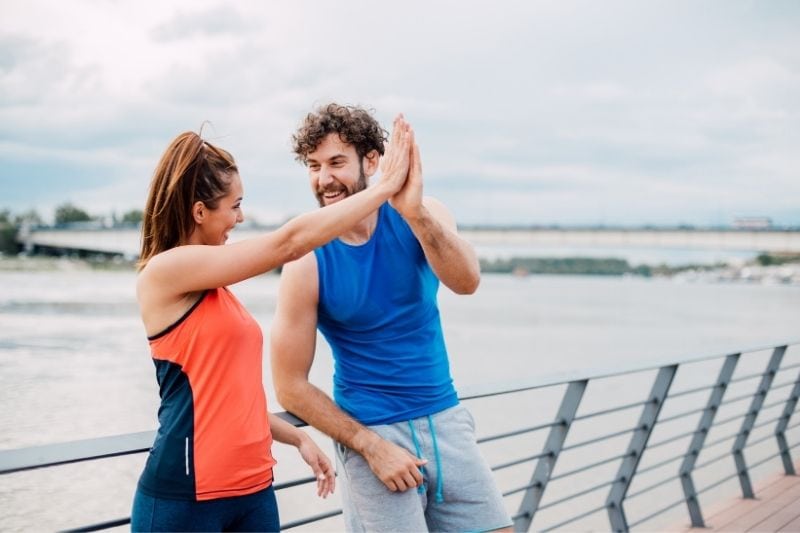 casal atlético a dar um "high five" um ao outro perto de uma massa de água