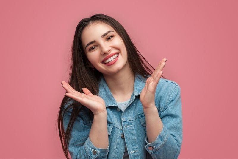 mulher sorridente e atraente a bater palmas, olhando para a câmara num fundo cor-de-rosa