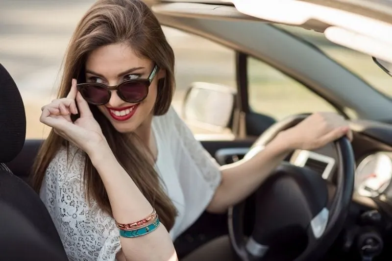 beautiful smiling woman riding a top down car looking at the back holding her sunglasses