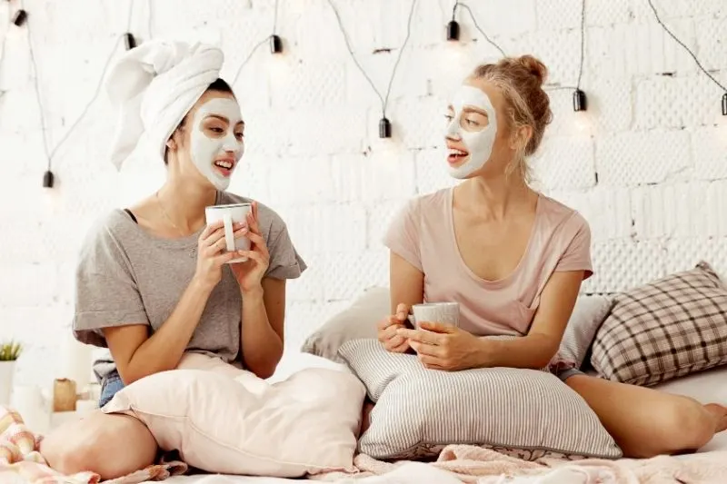 best friends talking with coffee insiding bedroom with face masks on their faces