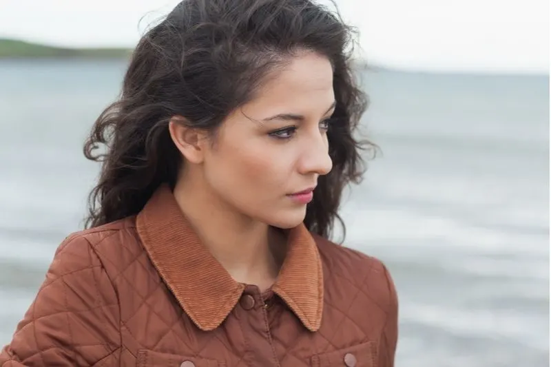 black haired woman thinking deeply and standing near the body of water
