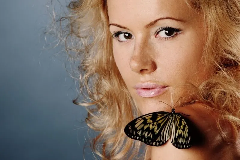 blonde woman with butterfly resting on her shoulder
