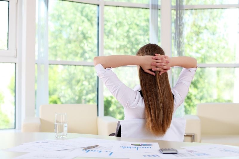 mulher de negócios a relaxar no escritório durante a pausa, virada para as janelas do escritório