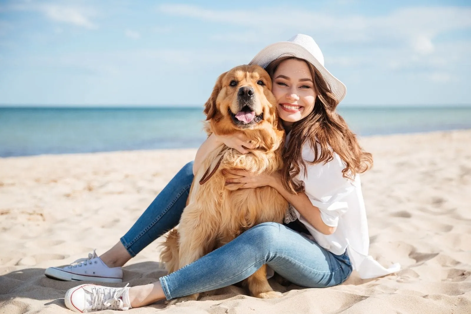 cheerful young woman sitting and embracing a dog in the beach during the day