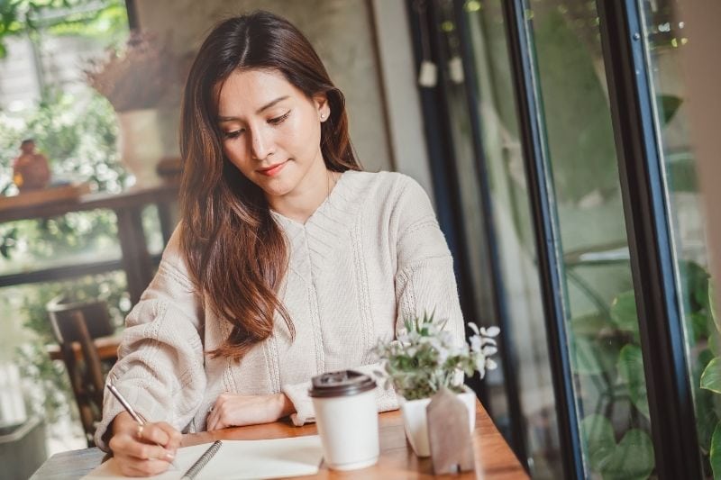 close up mujer asiática escribiendo en el cuaderno dentro de un café