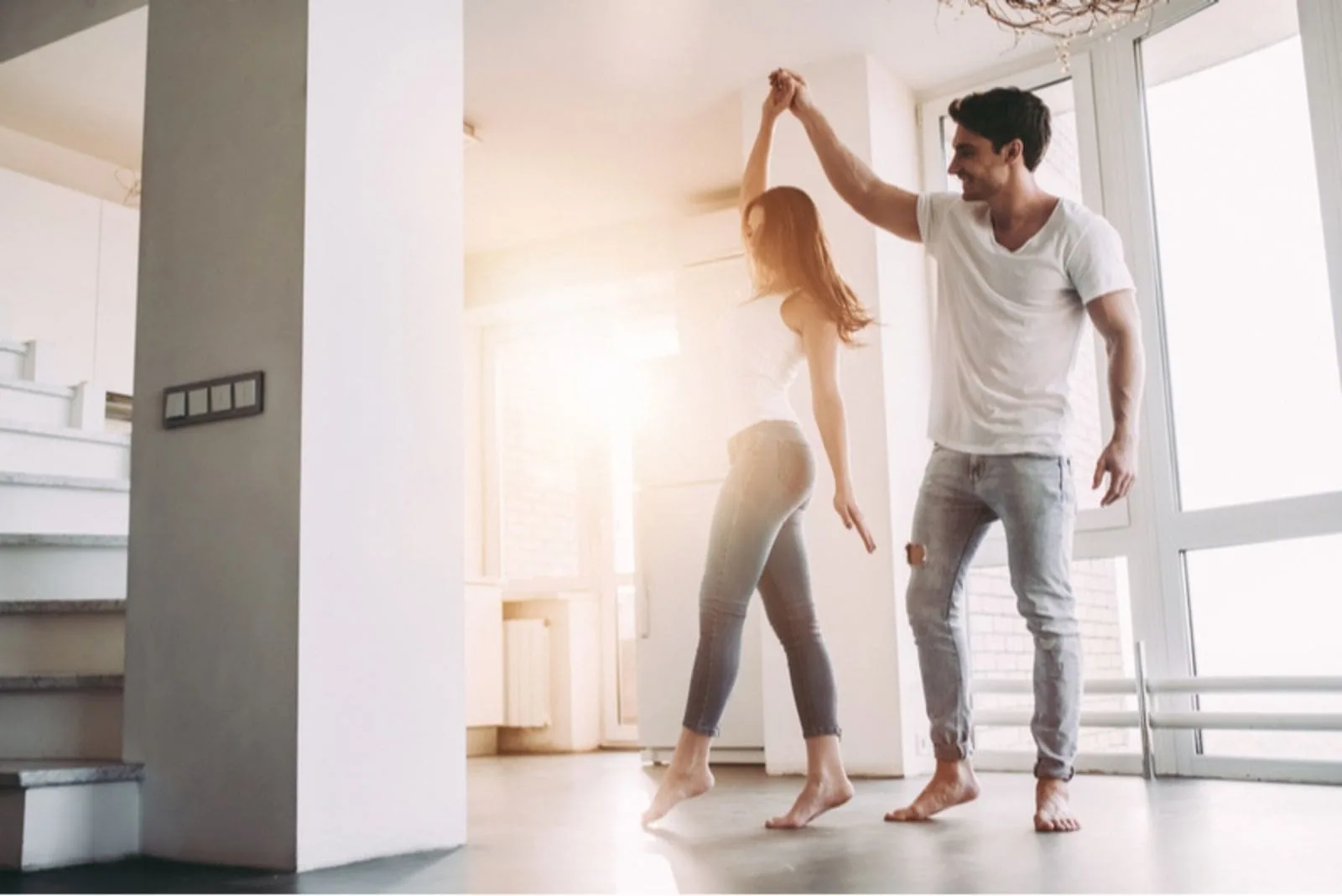 couple dancing around inside an empty room wearing white top and denim jeans