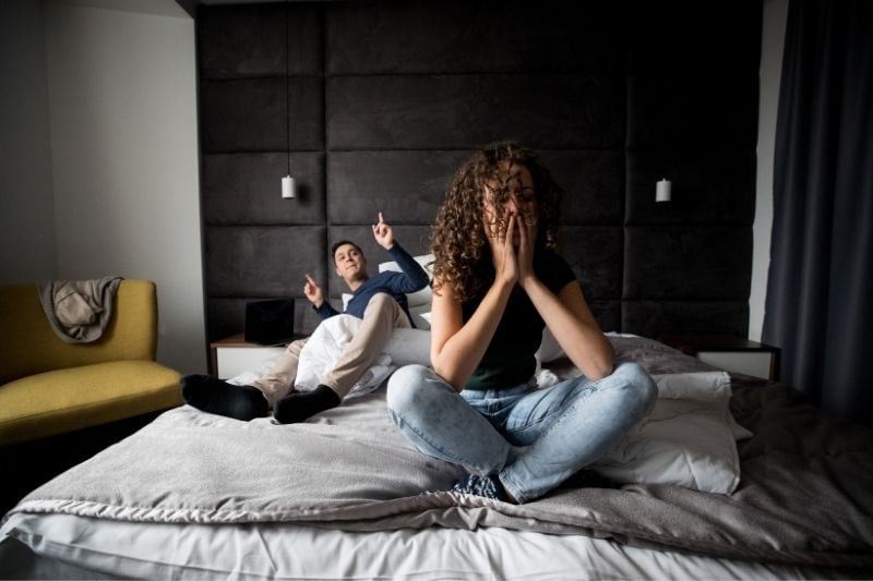 couple having problems fighting inside the bedroom while sitting on the bed with black headboard 