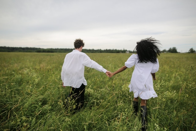 man and woman holding hands while walking on green grass field